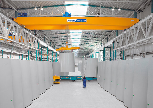 Suwnica pomostowa w hali przemysłowej przenosi duże ładunki, podczas gdy pracownik znajduje się w obszarze roboczym.