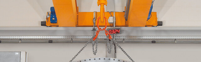 Belka wózka z nakładkami dzwignicy, do której przymocowany jest zawiesie łańcuchowe z ładunkiem.