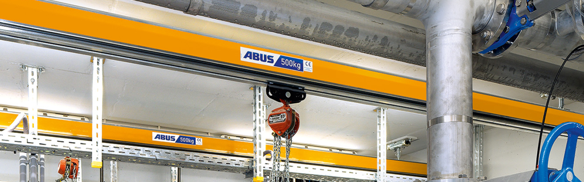 Jednoszynowa kolejka ABUS z wciągnikiem łańcuchowym w zakładzie przemysłowym, służąca do transportu ładunków.