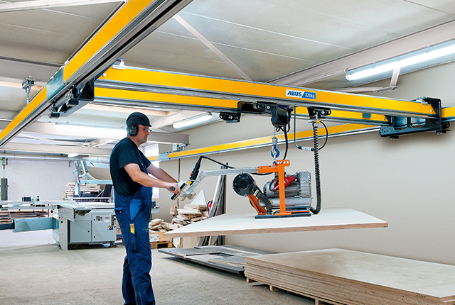 Pracownik obsługuje suwnicę dwudźwigarową typu ZHB-X i wykonuje podnoszenie ładunku za pomocą wciągnika łańcuchowego w hali produkcyjnej.