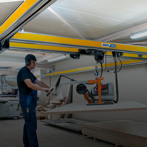 Pracownik obsługuje suwnicę dwudźwigarową typu ZHB-X i wykonuje podnoszenie ładunku za pomocą wciągnika łańcuchowego w hali produkcyjnej.