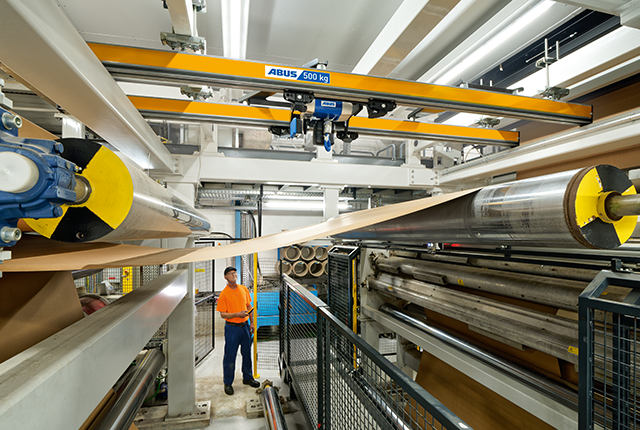 Kolejka dwuszynowa transportuje materiały wzdłuż linii produkcyjnej, podczas gdy pracownik nadzoruje proces.